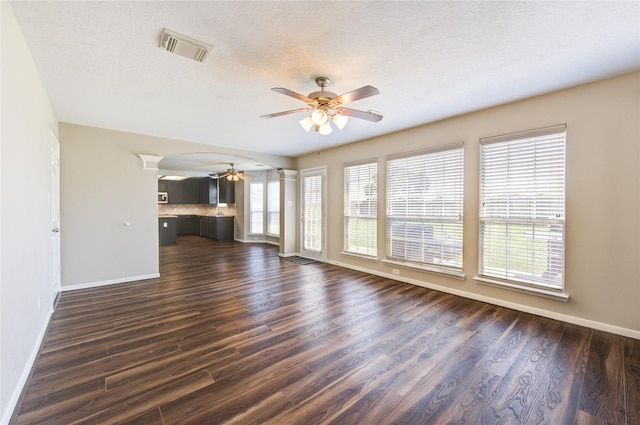 unfurnished living room with decorative columns, visible vents, ceiling fan, and dark wood-type flooring