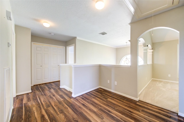 empty room with a textured ceiling, visible vents, baseboards, dark wood finished floors, and attic access