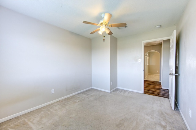 empty room featuring arched walkways, carpet flooring, a ceiling fan, baseboards, and attic access