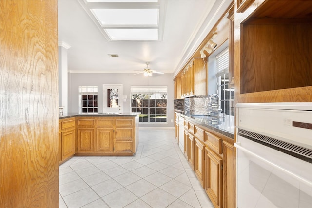 kitchen with white oven, crown molding, light tile patterned floors, a sink, and ceiling fan