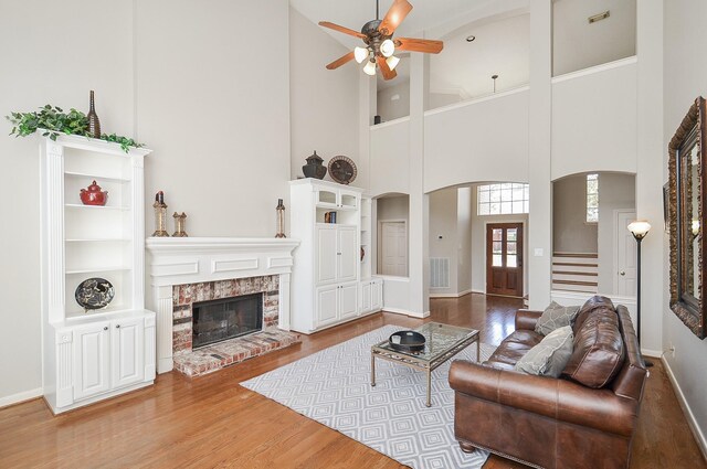 living area with visible vents, ceiling fan, a fireplace, wood finished floors, and arched walkways