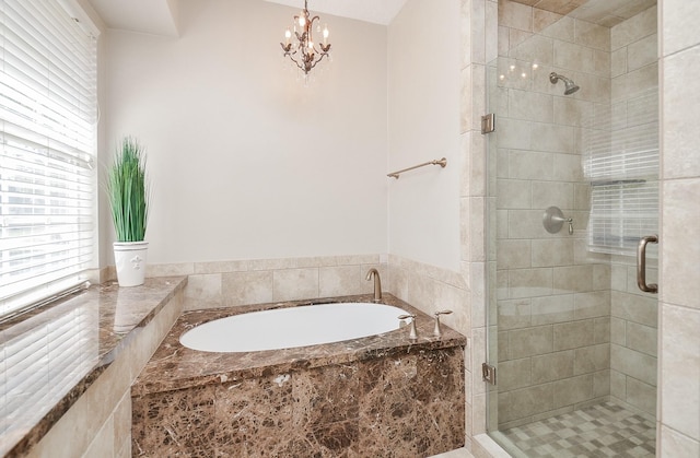 bathroom with a garden tub, a notable chandelier, and a stall shower