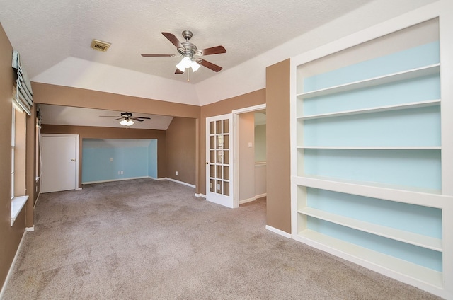 empty room with built in features, visible vents, carpet flooring, and a ceiling fan