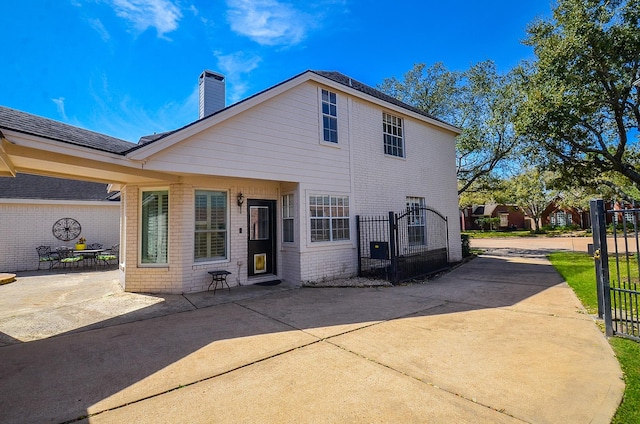 rear view of house with concrete driveway, a gate, fence, and brick siding