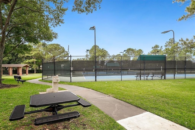 view of home's community featuring a tennis court, a lawn, and fence