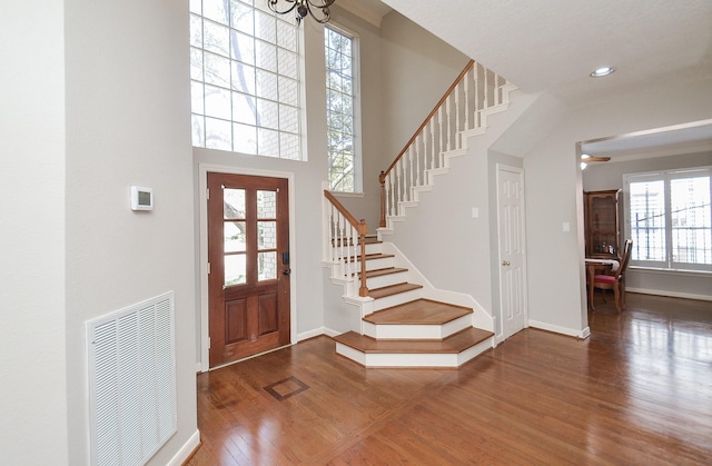 foyer entrance with visible vents, wood finished floors, baseboards, a towering ceiling, and stairs