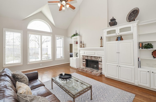 living room featuring wood finished floors, a brick fireplace, a ceiling fan, and high vaulted ceiling