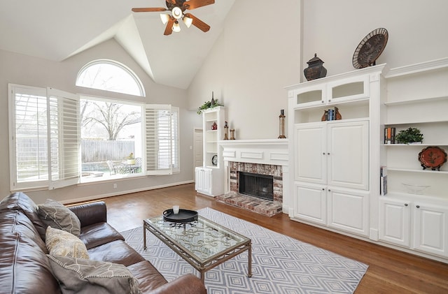 living room featuring a brick fireplace, wood finished floors, high vaulted ceiling, and ceiling fan