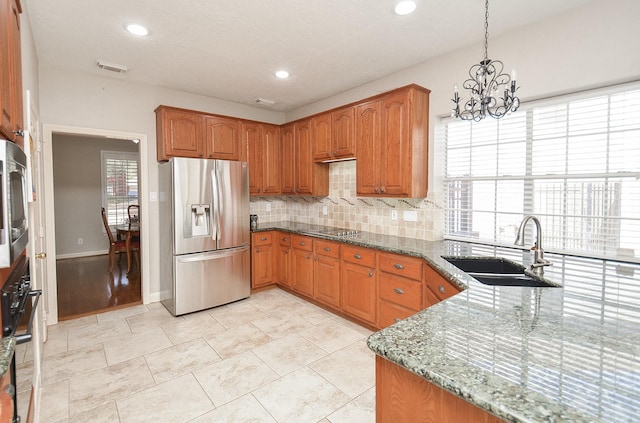 kitchen with stone countertops, a sink, black appliances, a notable chandelier, and tasteful backsplash