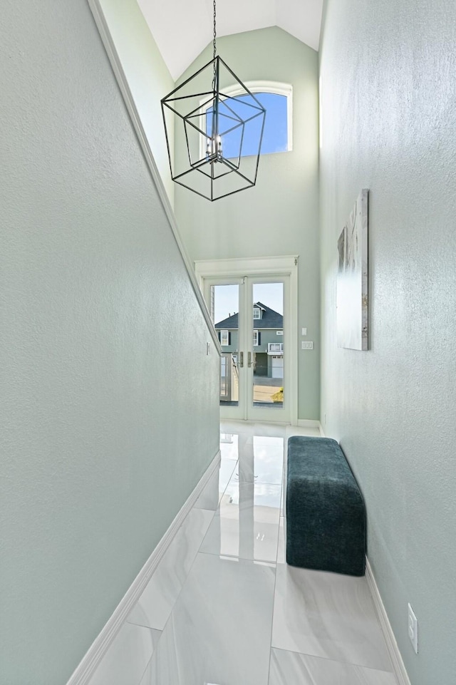 hallway featuring a chandelier, high vaulted ceiling, baseboards, marble finish floor, and french doors