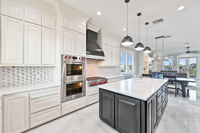 kitchen with a center island, marble finish floor, stainless steel appliances, white cabinetry, and wall chimney exhaust hood