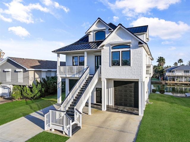 coastal home with a front yard, concrete driveway, stairway, and a standing seam roof