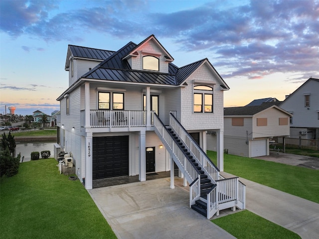 coastal inspired home featuring a garage, stairs, driveway, a lawn, and a standing seam roof