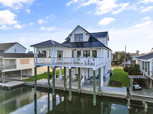 rear view of property with a yard, a standing seam roof, a water view, and metal roof