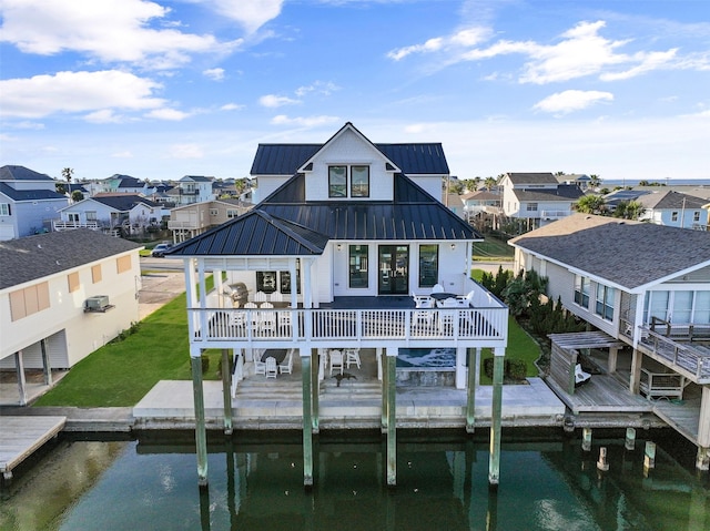 back of house featuring a standing seam roof, a residential view, metal roof, and a deck with water view