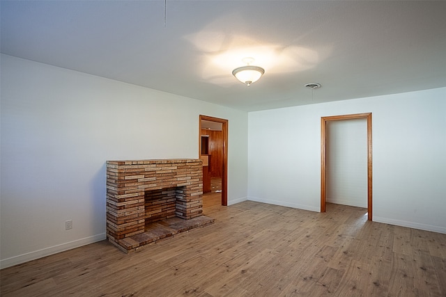 unfurnished living room featuring baseboards, a fireplace with raised hearth, and wood finished floors