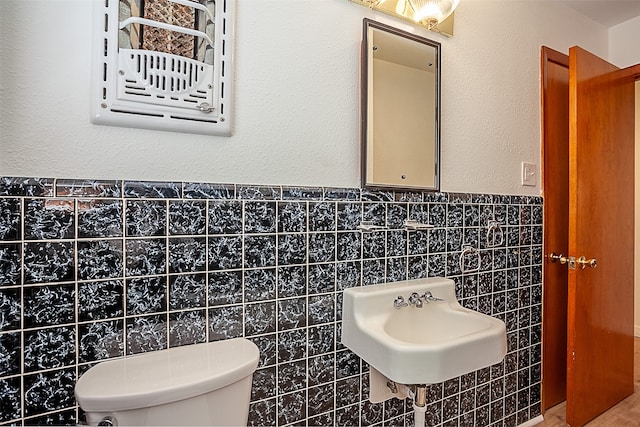 bathroom with toilet, a sink, tile walls, and wainscoting