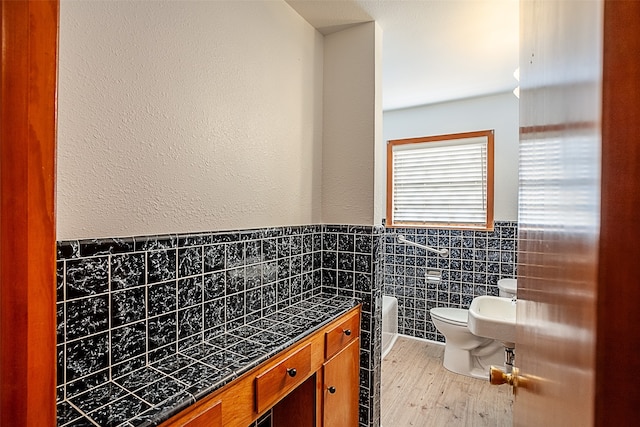 bathroom with toilet, tile walls, wood finished floors, and wainscoting