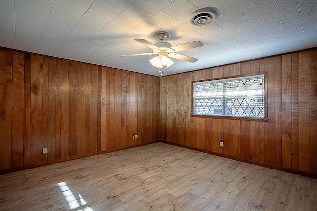 empty room with baseboards, visible vents, a ceiling fan, wood finished floors, and wood walls