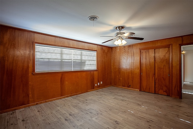 unfurnished room featuring wood walls, a ceiling fan, visible vents, and wood finished floors