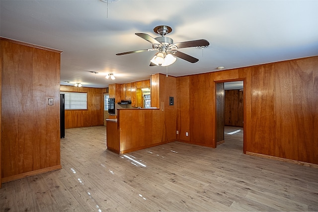 kitchen with wooden walls, brown cabinets, ceiling fan, and light wood-style flooring