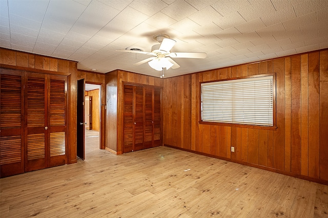 unfurnished bedroom featuring baseboards, a ceiling fan, hardwood / wood-style flooring, wood walls, and multiple closets