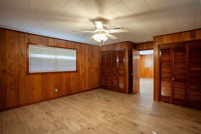 empty room with light wood-style floors, ceiling fan, wooden walls, and baseboards