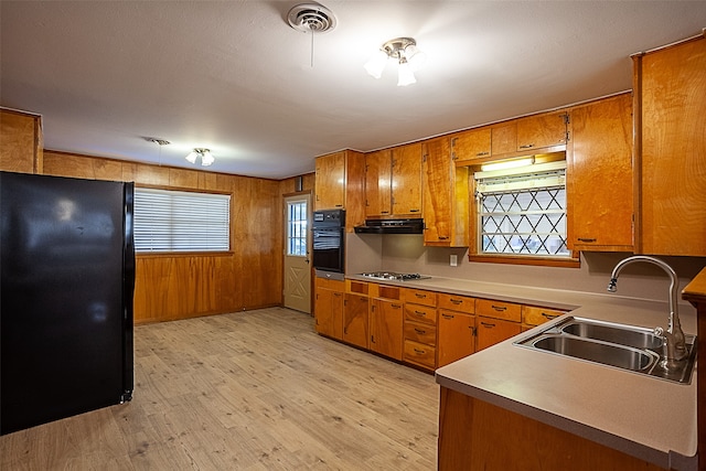 kitchen with light wood finished floors, visible vents, brown cabinetry, a sink, and under cabinet range hood