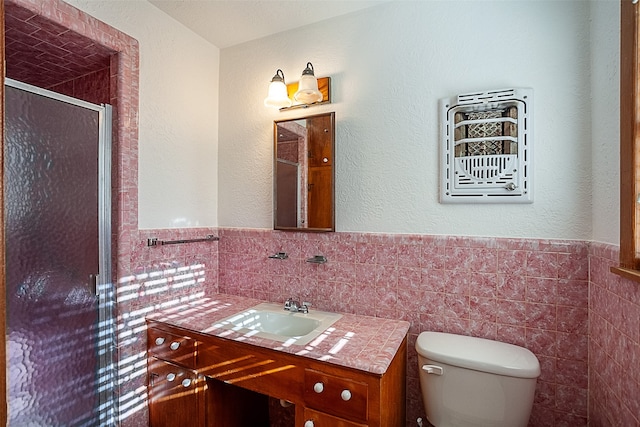 bathroom with toilet, a wainscoted wall, vanity, a shower stall, and tile walls