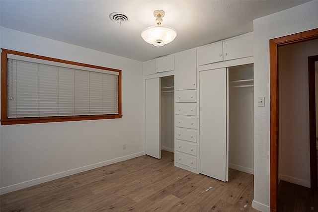 unfurnished bedroom with multiple closets, light wood-type flooring, visible vents, and baseboards