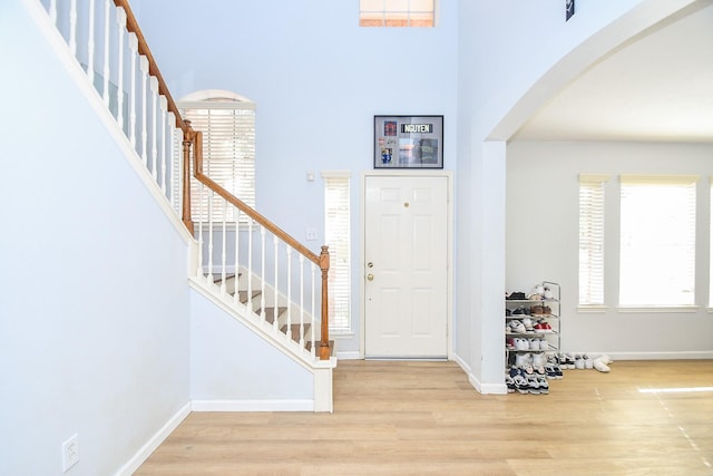 foyer with arched walkways, wood finished floors, stairs, and baseboards