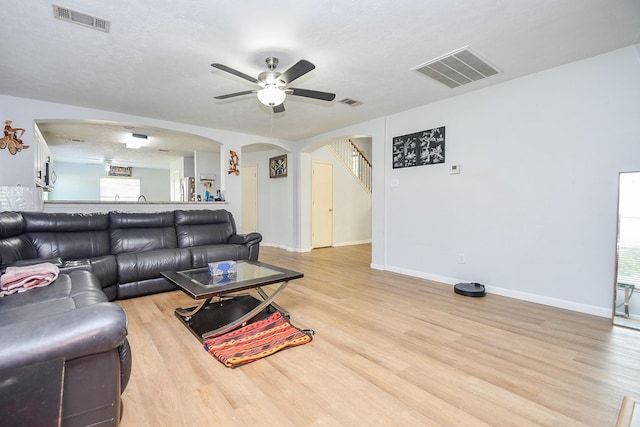 living area with arched walkways, visible vents, light wood-style flooring, and baseboards