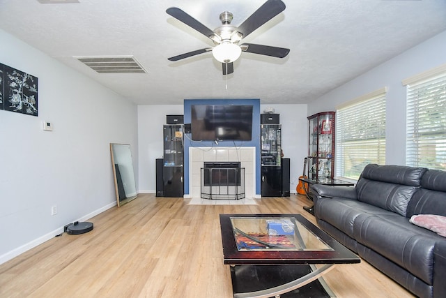 living area with a textured ceiling, a fireplace, wood finished floors, visible vents, and baseboards