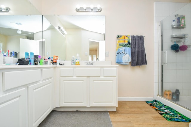 bathroom featuring double vanity, a stall shower, baseboards, wood finished floors, and a sink