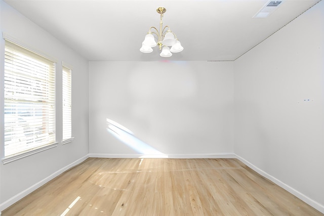 empty room with a chandelier, baseboards, visible vents, and light wood finished floors