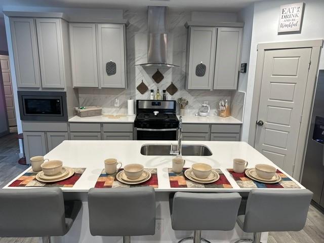 kitchen featuring a sink, stainless steel appliances, gray cabinetry, wall chimney range hood, and backsplash