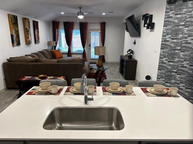 kitchen featuring light countertops, open floor plan, vaulted ceiling, a sink, and ceiling fan