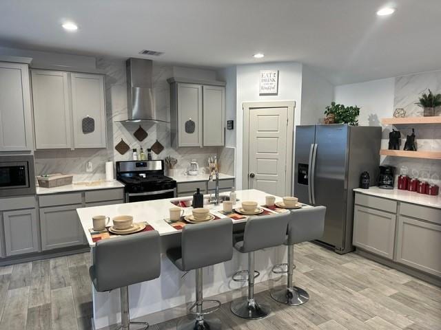 kitchen with appliances with stainless steel finishes, wall chimney exhaust hood, backsplash, and gray cabinetry