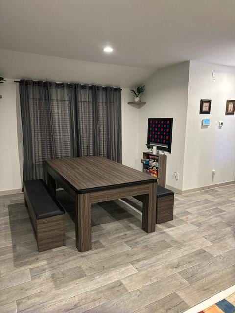 dining area featuring light wood-type flooring, baseboards, and lofted ceiling