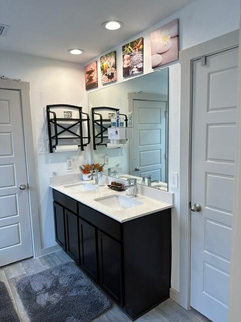 full bath with double vanity, wood finished floors, a sink, and visible vents