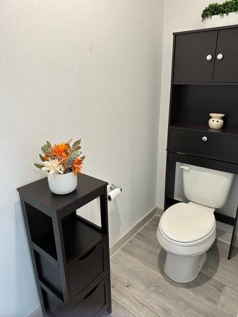 bathroom featuring a textured wall, wood finished floors, toilet, and baseboards