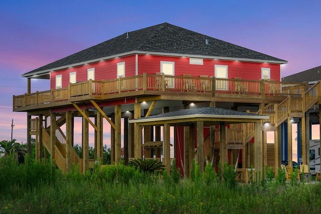 back of property at dusk featuring stairs, a deck, and roof with shingles