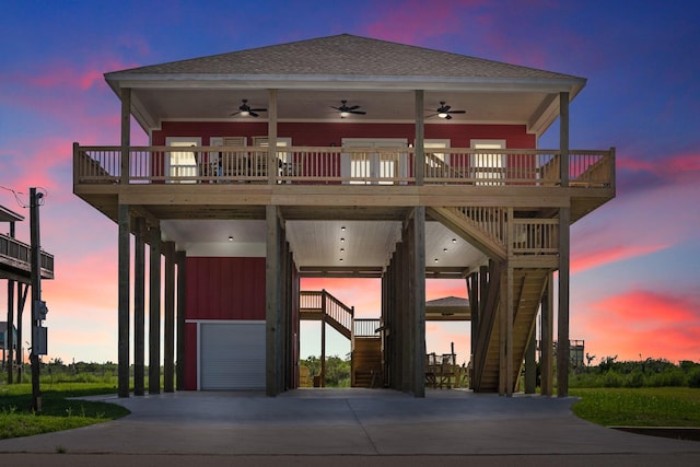 coastal home with ceiling fan, roof with shingles, a deck, and stairway