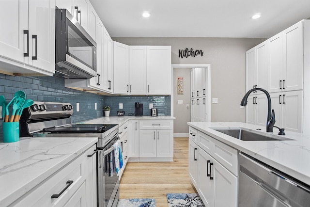 kitchen featuring light wood finished floors, white cabinets, a sink, stainless steel appliances, and backsplash