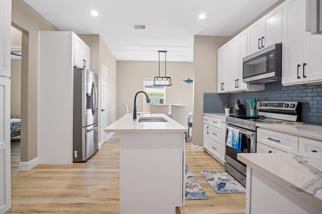 kitchen featuring a kitchen island with sink, a sink, visible vents, appliances with stainless steel finishes, and light wood-type flooring