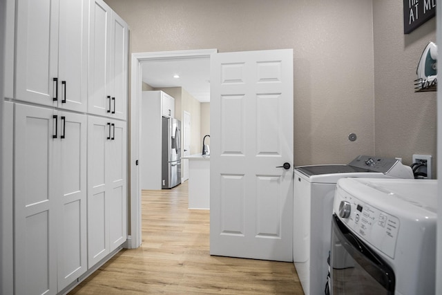 laundry room featuring a textured wall, a sink, light wood-style floors, cabinet space, and washing machine and clothes dryer