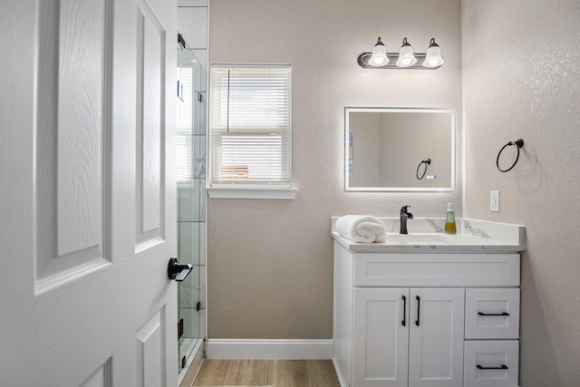 bathroom with a textured wall, wood finished floors, vanity, baseboards, and a stall shower