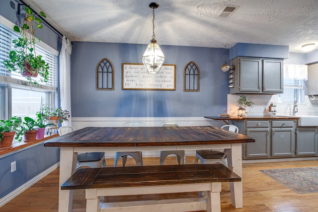 dining area featuring visible vents, a wainscoted wall, a textured ceiling, and light wood-style flooring