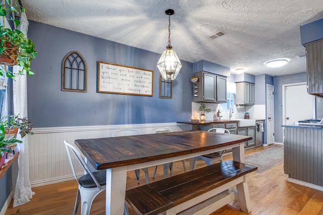 dining space featuring light wood-type flooring, visible vents, a textured ceiling, and wainscoting