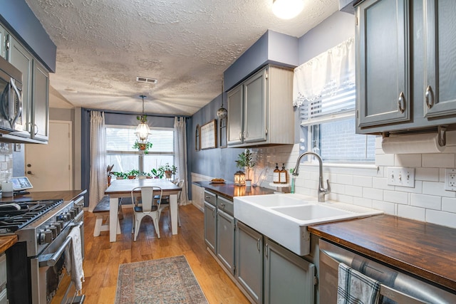 kitchen featuring tasteful backsplash, light wood-style flooring, appliances with stainless steel finishes, a textured ceiling, and a sink